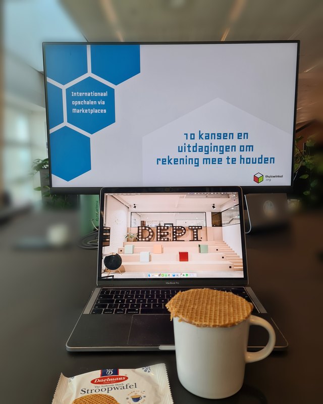 A stroopwafel warming on a cup of coffee next to a laptop, moments before a keynote